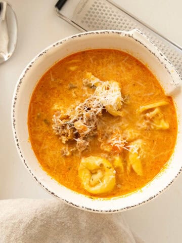 Rustic Italian tortellini soup with sausage in a bowl topped with parmesan cheese.