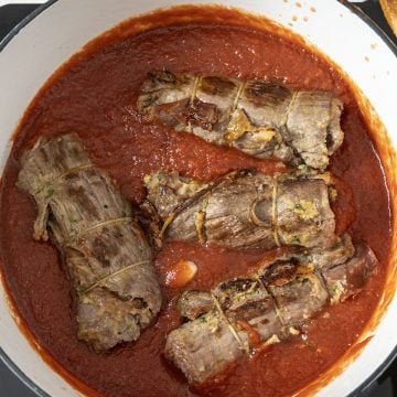 Braciole added to tomato sauce covered about half way to braise