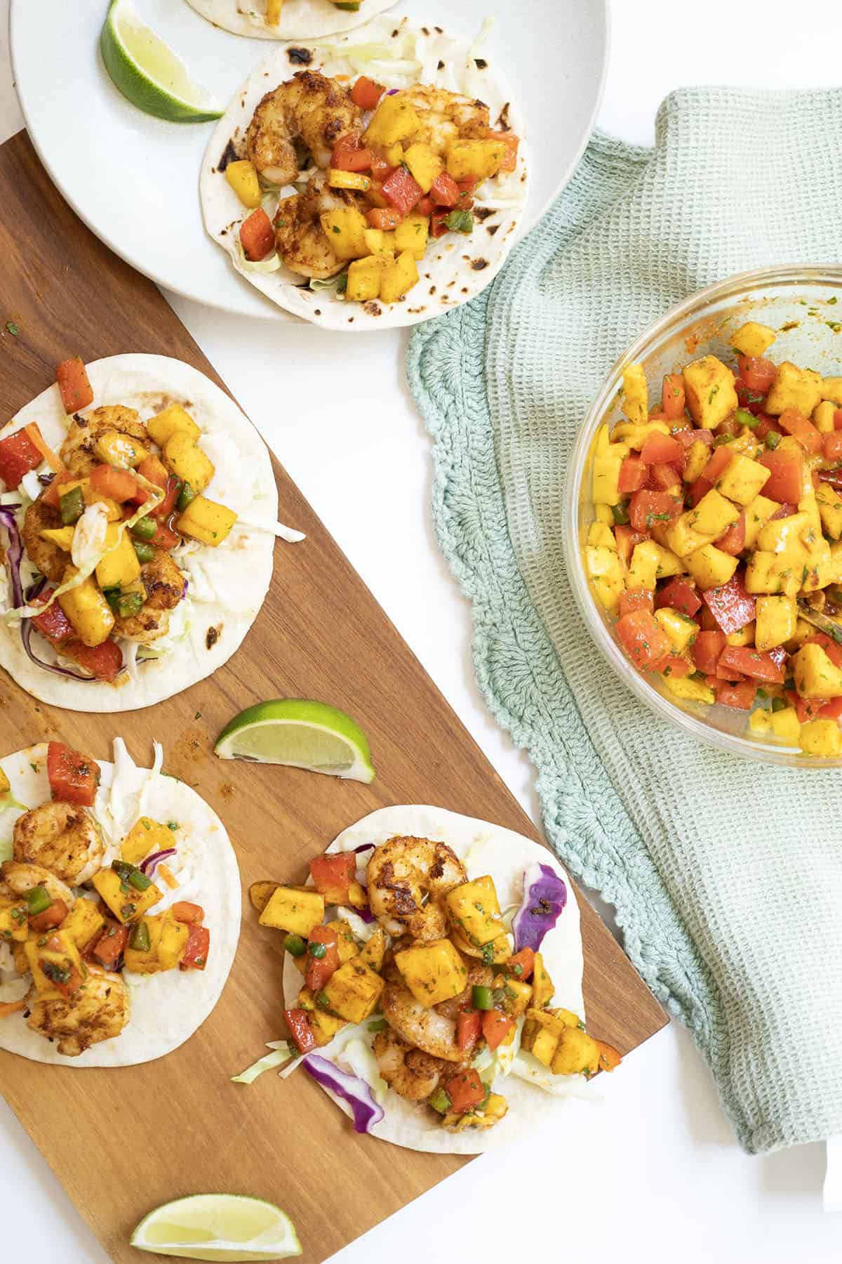 three shrimp tacos on white flour tortillas topped with mango salsa with a lime wedge in the middle.