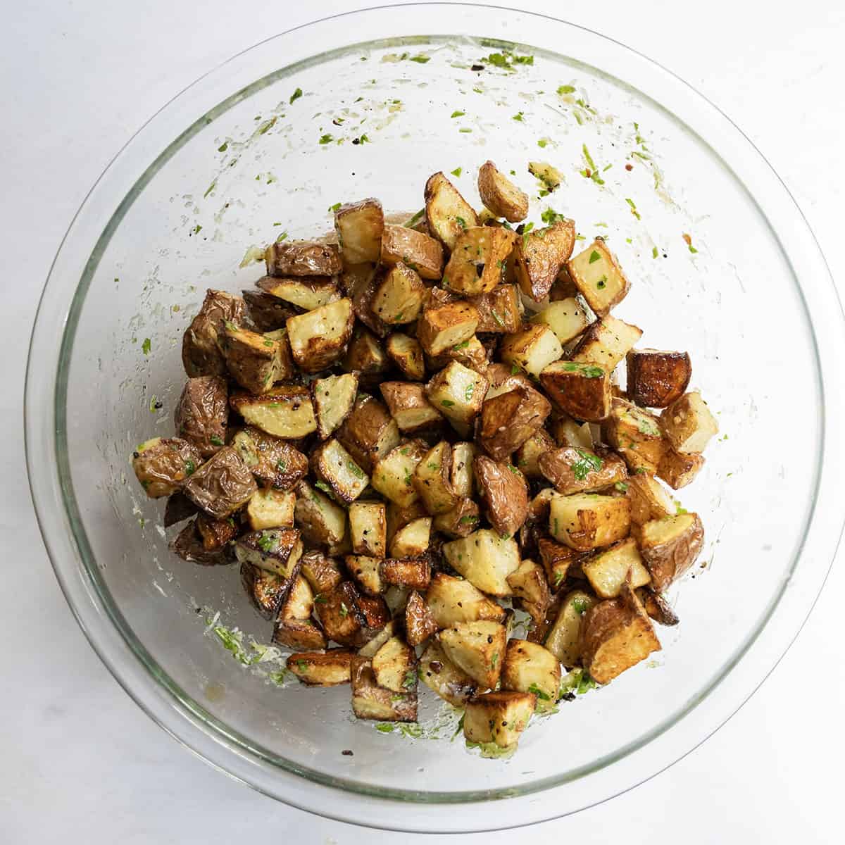 Crispy potatoes being tossed in dressing and parmesan.