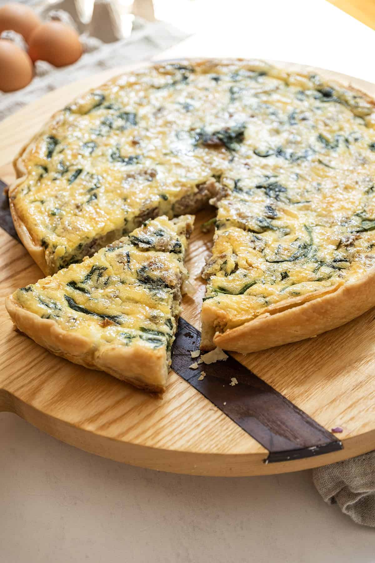 sausage and cheese quiche on a cutting board with one slice cut out.