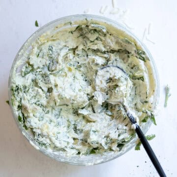 Cheese mixed with spinach and artichokes in a bowl.