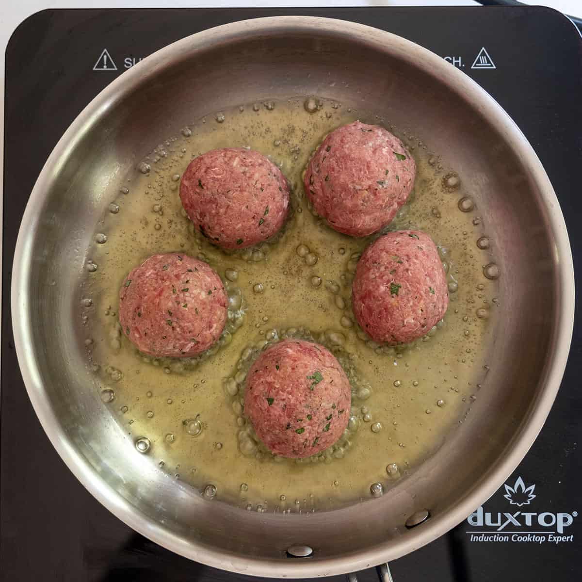 meatballs frying in frying pan.
