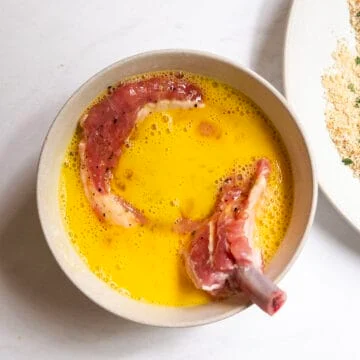Pork chop in bowl of whisked egg.
