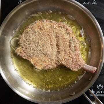 Pork chop in a frying pan frying in olive oil.