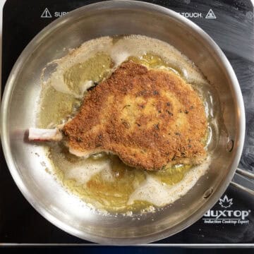 Pork chop flipped over in frying pan with golden brown coating.
