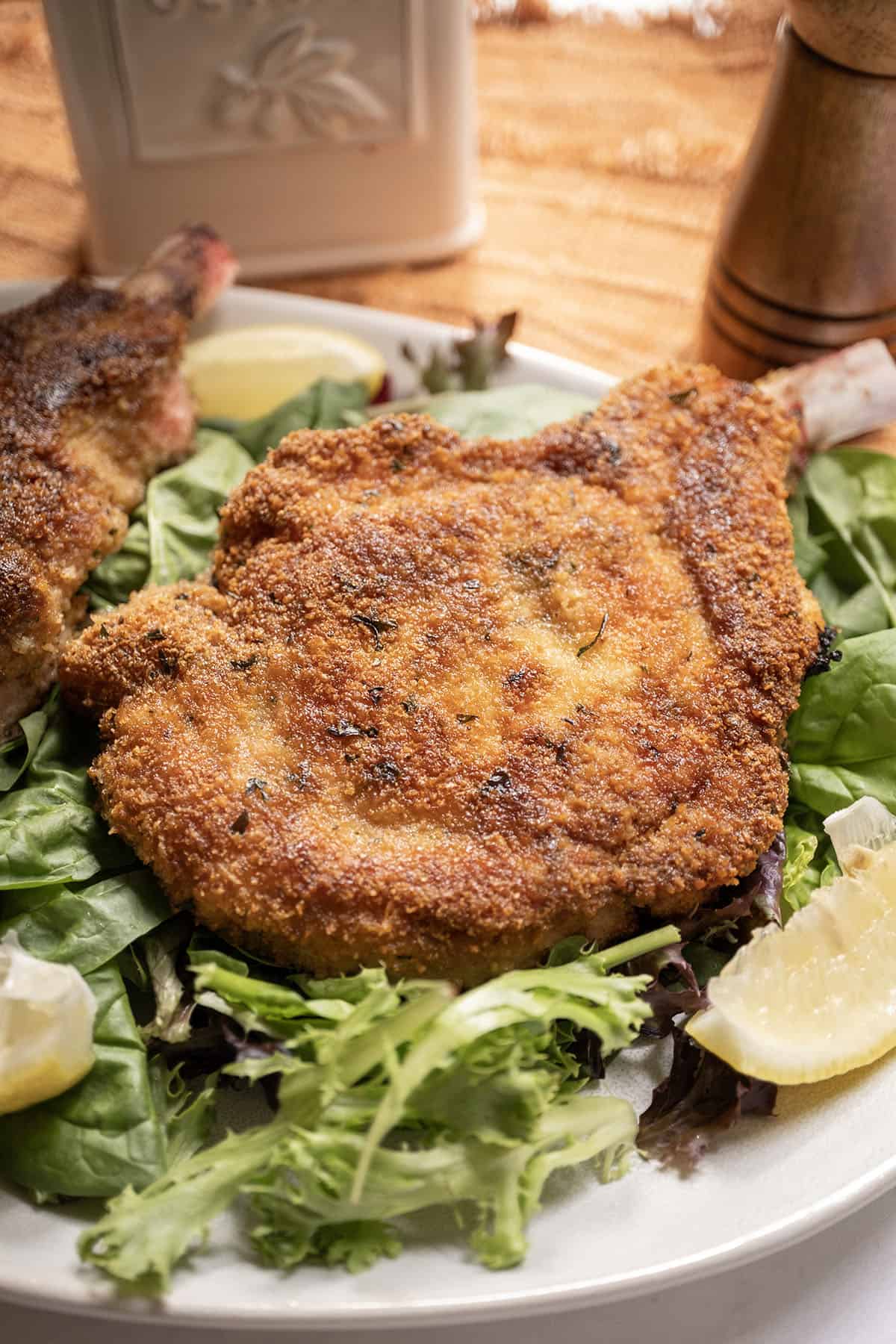 Pork chop milanese over a greens salad and a wedge of lemon on the side.