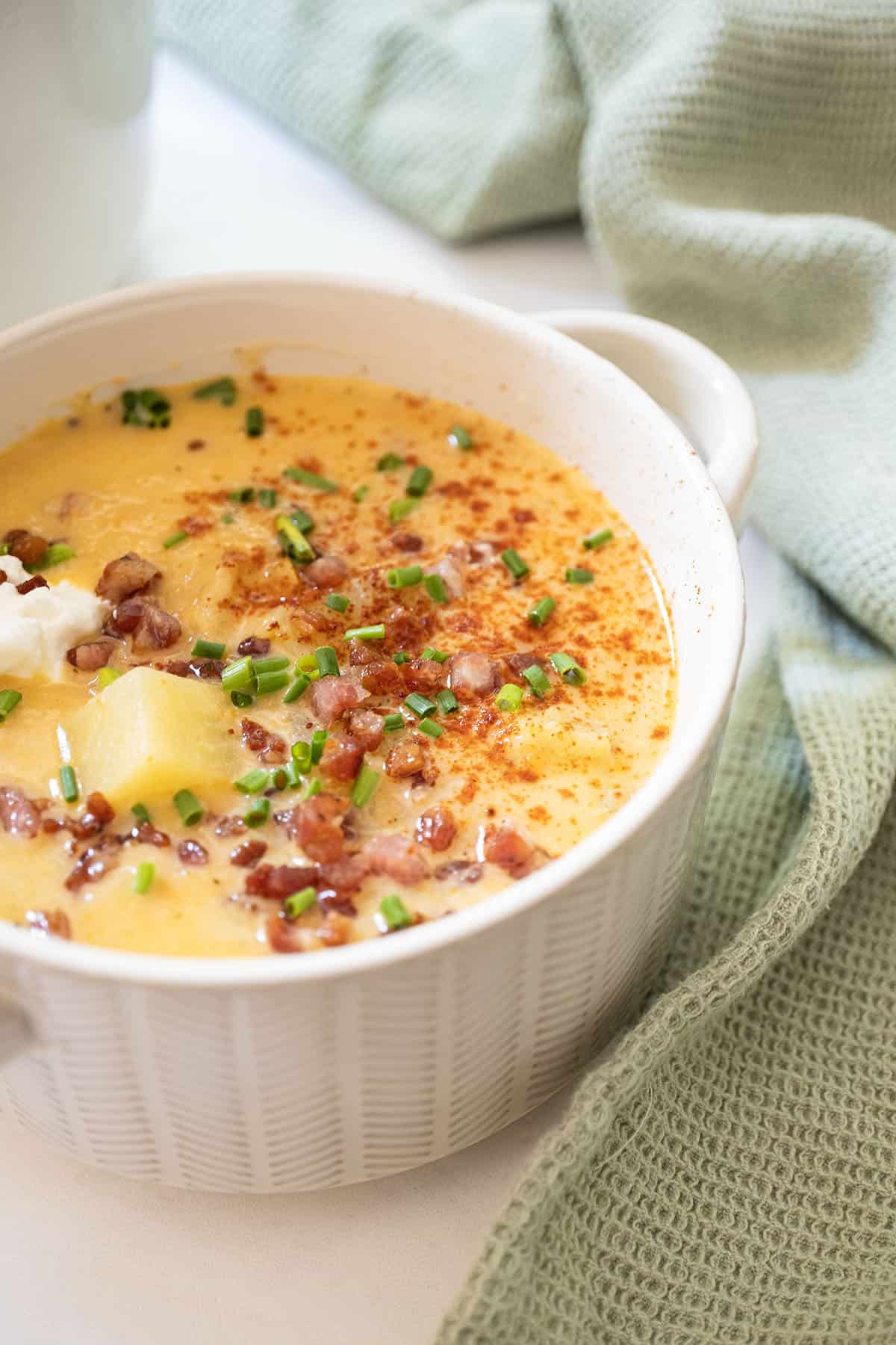 Creamy potato and onion soup topped with pancetta, chives, and sour cream next to the pot of soup.