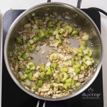 Sauteed celery, onion, and mushroom stems in a pan.