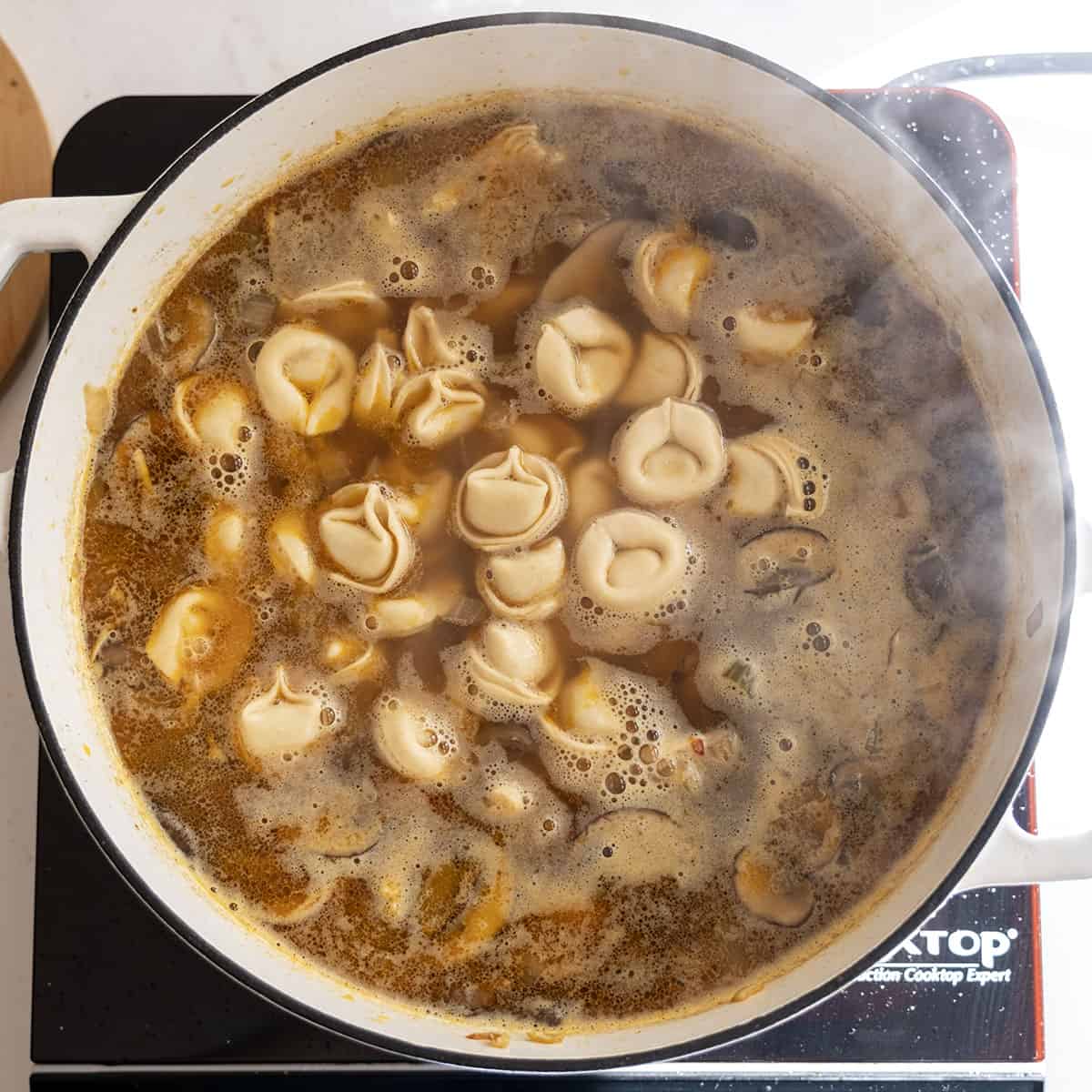 Soup simmering in the pot with tortellini floating on top.