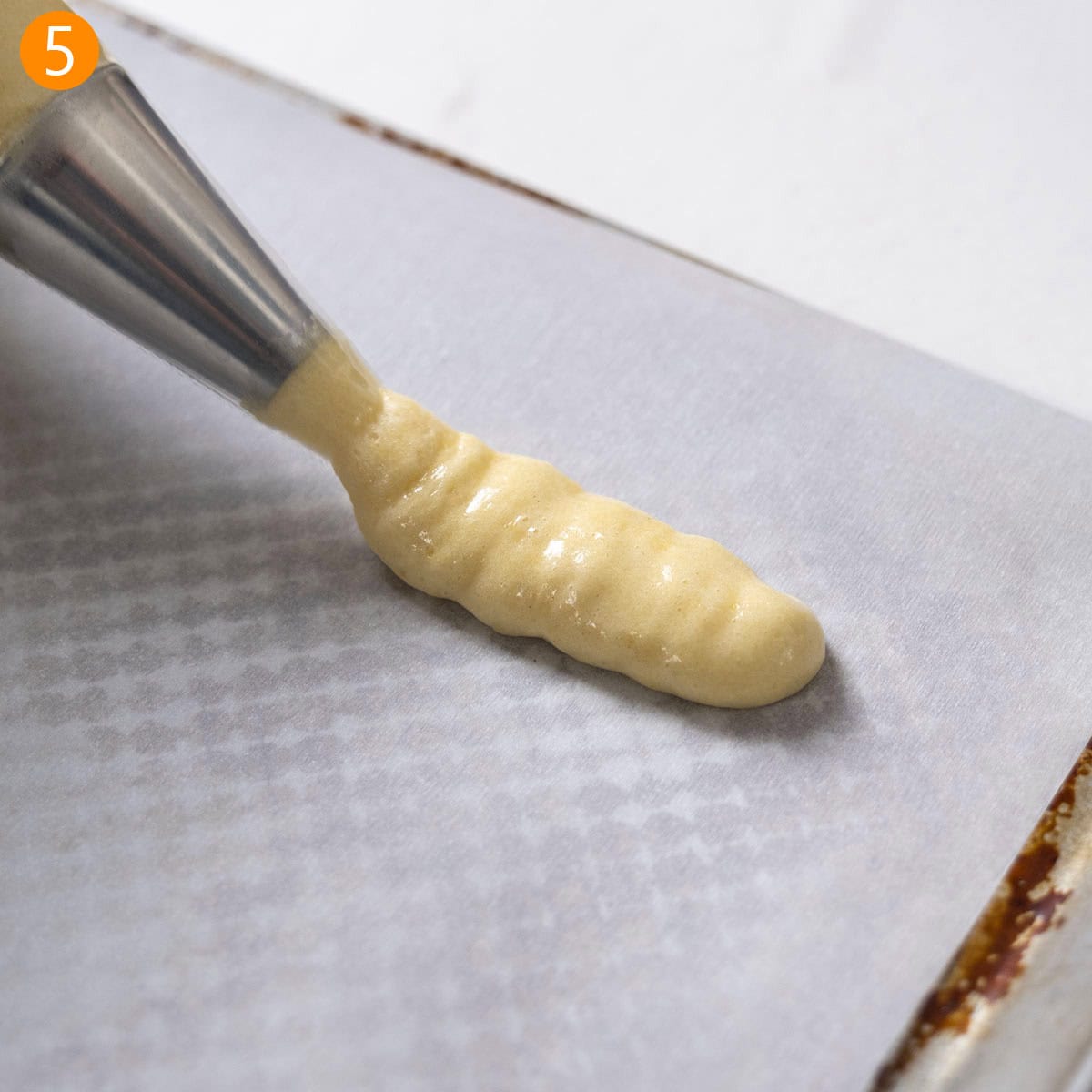 Piping the batter onto the parchment paper.