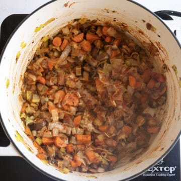 Sauteing vegetables with tomato paste caramelizing in a pot.