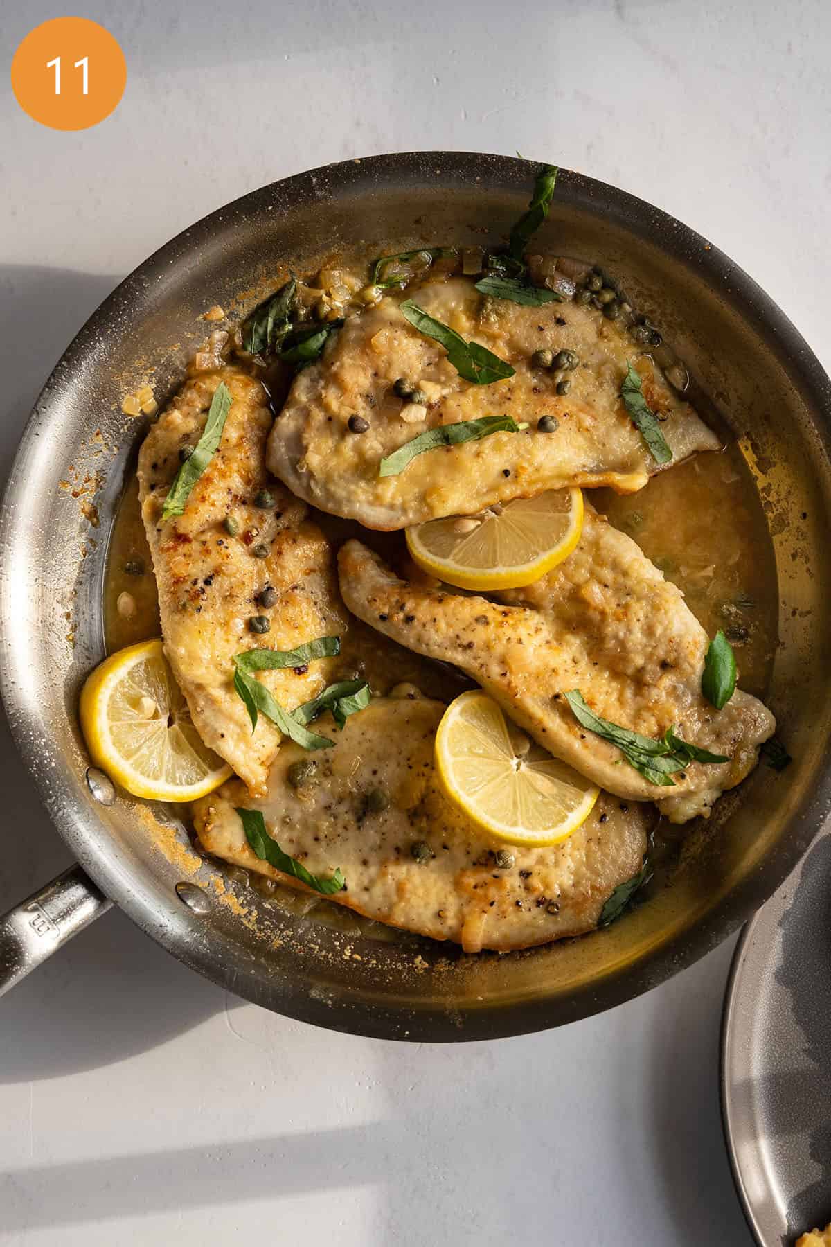 Chicken piccata in sauce pan topped with basil and capers.