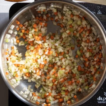 Carrots, onion, and celery sauteing in a saucepan.