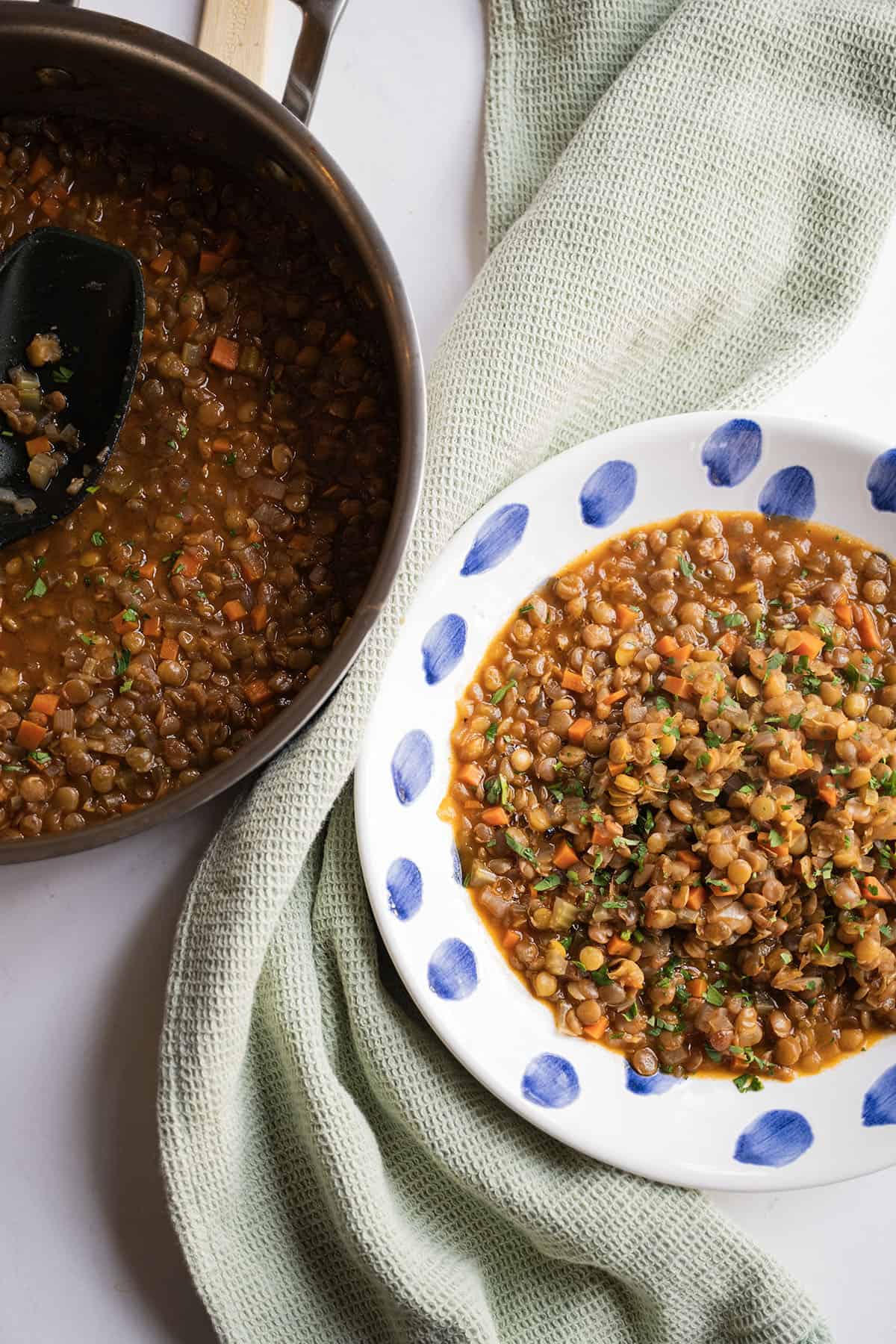 Cooked lentils in a bowl next to saucepan of lentils.