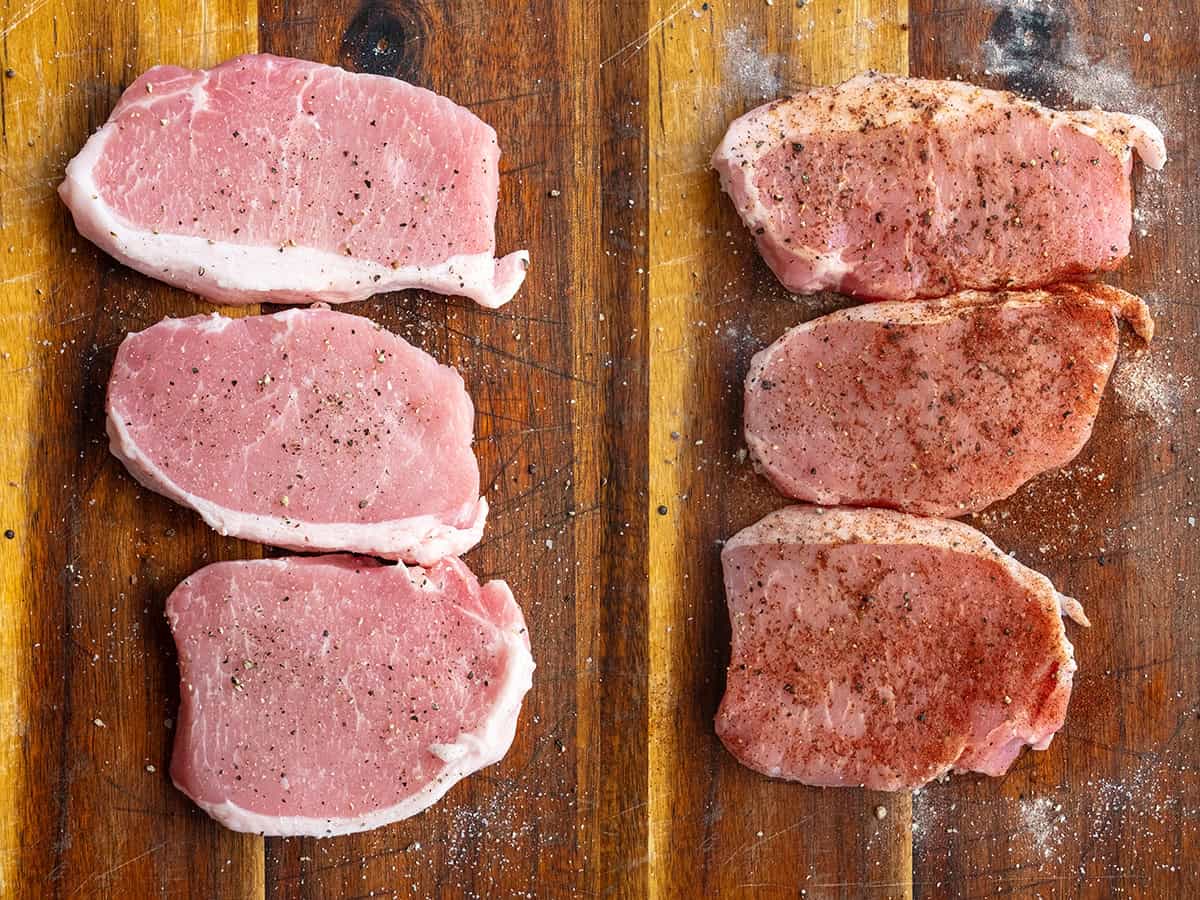 Seasoning pork chops on a cutting board.
