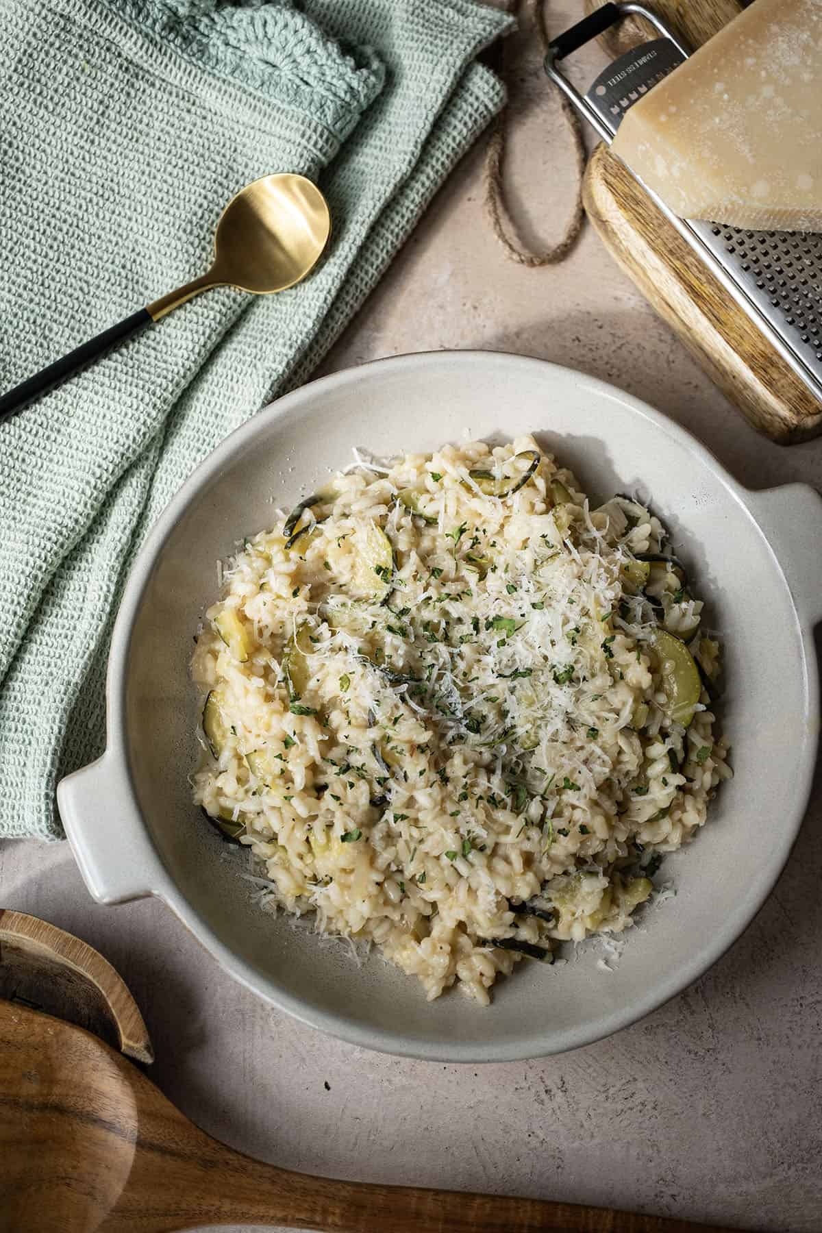 Zucchini risotto in a bowl topped with parmigiano and parsley.