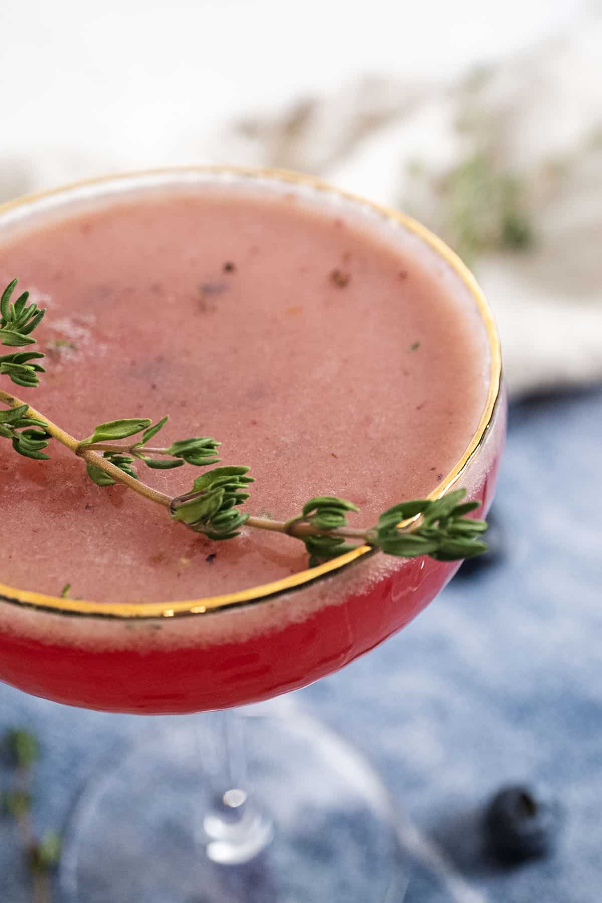 Blueberry mocktail with a sprig of thyme garnish in a glass.