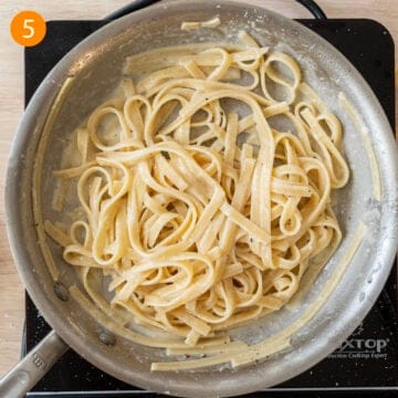 Parmigiano cheese added to pasta in pan.