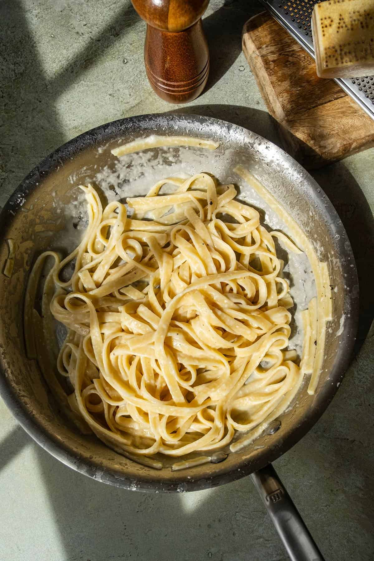 Fettucine alfredo in a pan with parmigiano and pepper on the side.