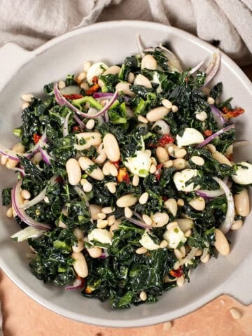 Kale and Cannellini Bean salad in a bowl topped with pine nuts.