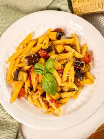 Pasta with eggplant and cherry tomatoes in a bowl garnished with fresh basil.