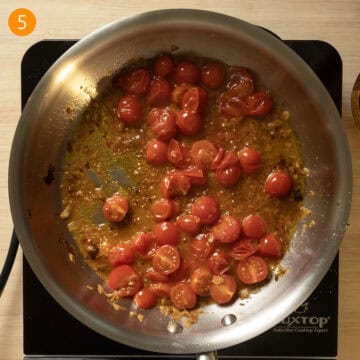 Cherry tomatoes breaking down in a pan and wine sauce thickening.