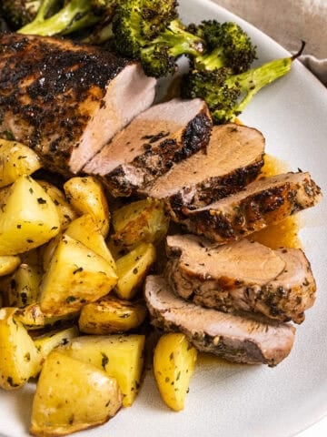 Sliced pork tenderloin served on a plate with roasted potatoes and broccoli.