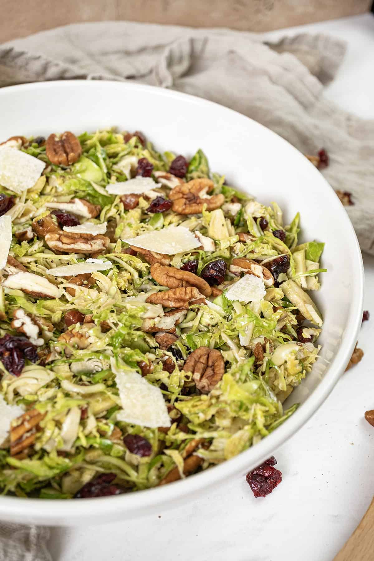 Brussels sprouts salad in a bowl topped with dried cranberries and pecans.