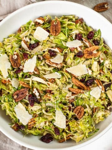 Brussels sprouts salad in a bowl topped with dried cranberries and pecans.