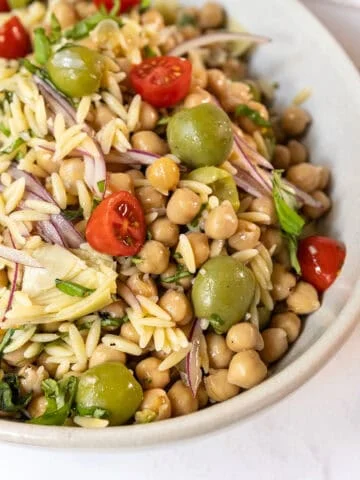 Orzo and garbanzo bean salad with olives, tomatoes, and more in a bowl.
