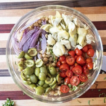 Adding tomatoes, olives, red onion and artichokes into the bowl.