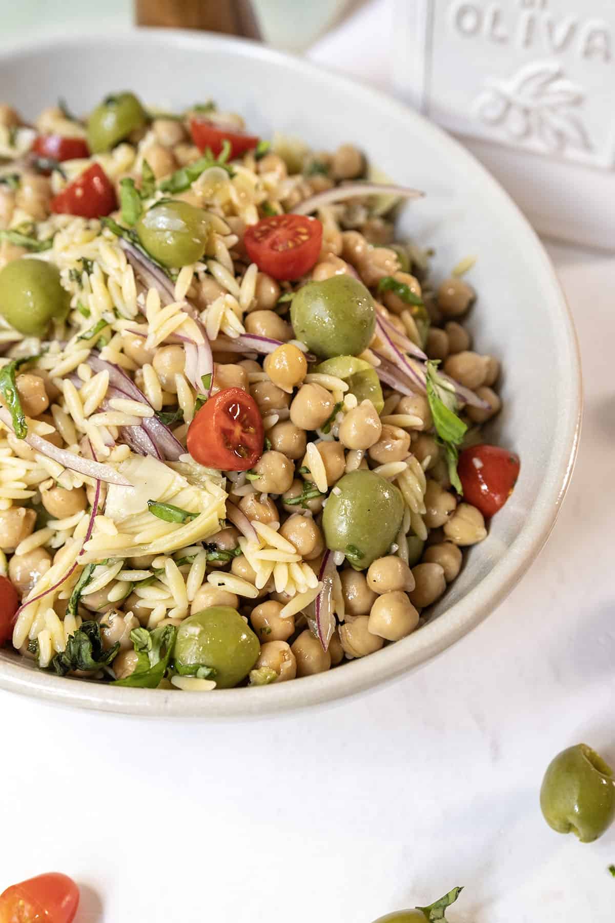 Orzo and garbanzo bean salad with olives, tomatoes, and more in a bowl.