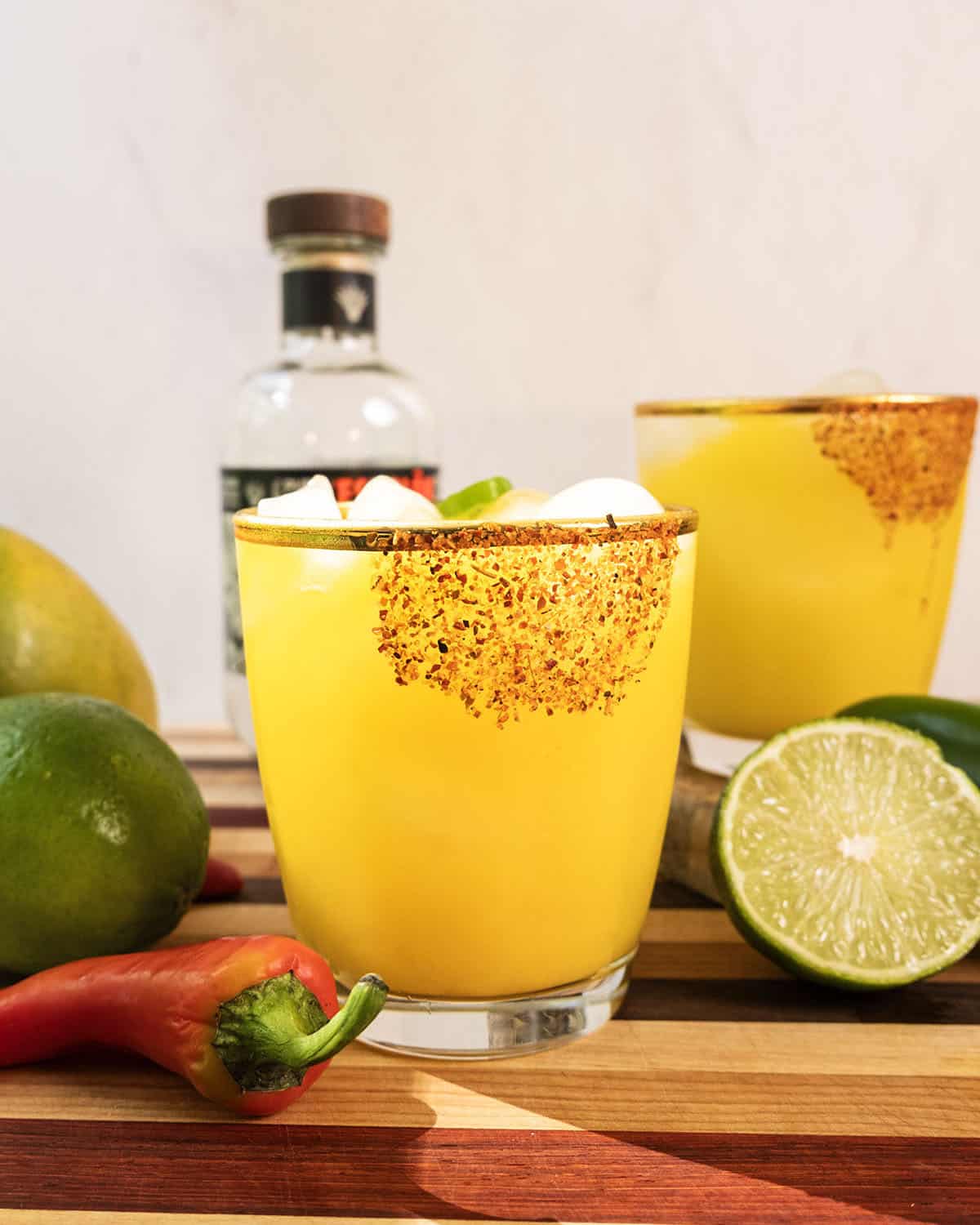 Spicy mango margarita with several jalapenos and limes surrounding it.