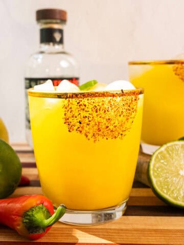 Spicy mango margarita with several jalapenos and limes surrounding it.