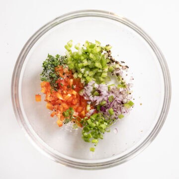 Combining fresh chopped veggies in a bowl with lemon, salt, and pepper.