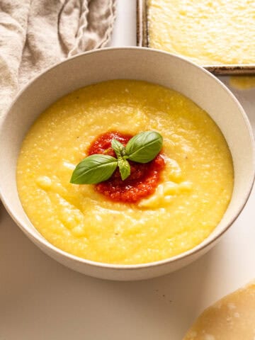 Creamy polenta in a bowl topped with marinara and basil.