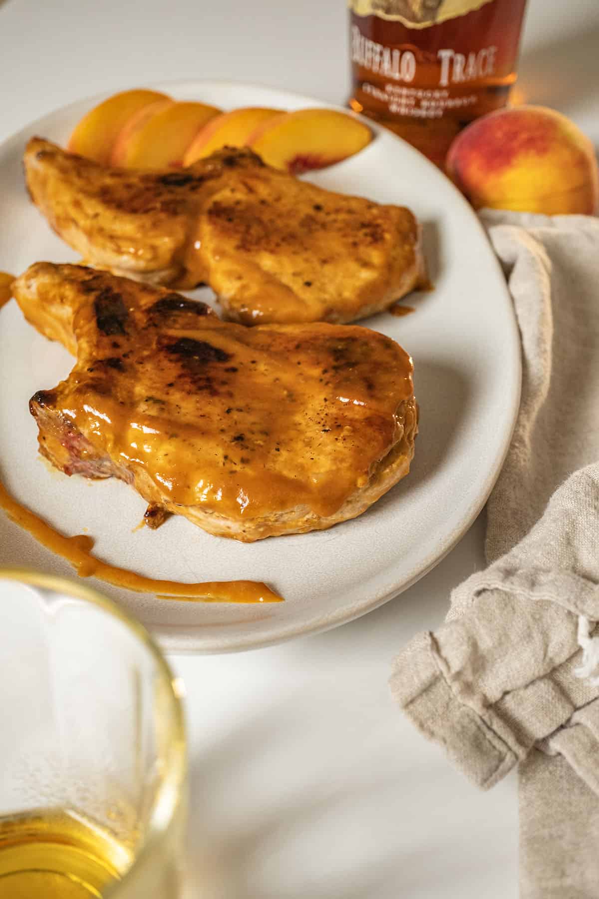 Bourbon peach glazed pork chops on a plate garnished with peaches and extra sauce.