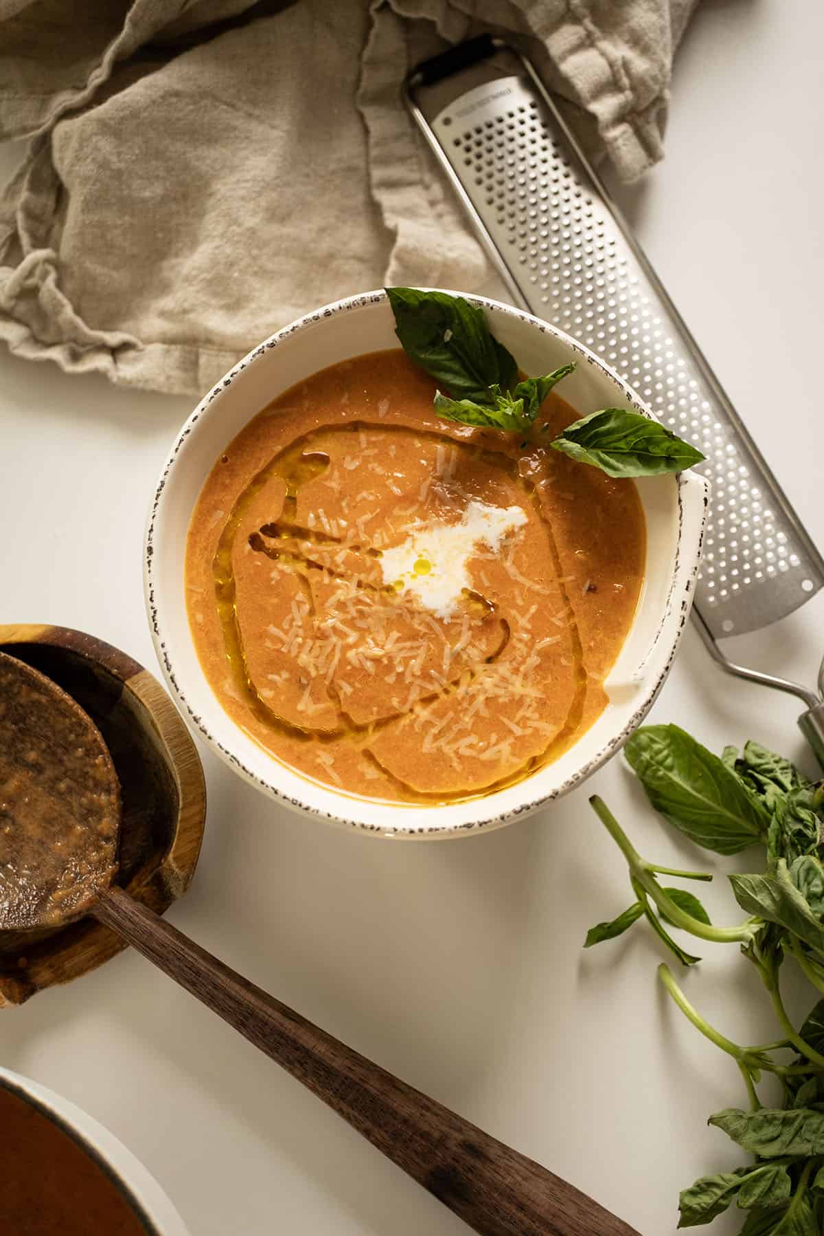 Tomato soup in a bowl topped with cream, olive oil, and basil.
