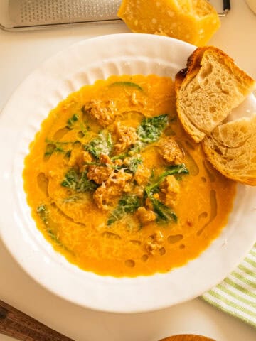 Butternut squash soup with sausage in a bowl and side of crusty Italian bread.