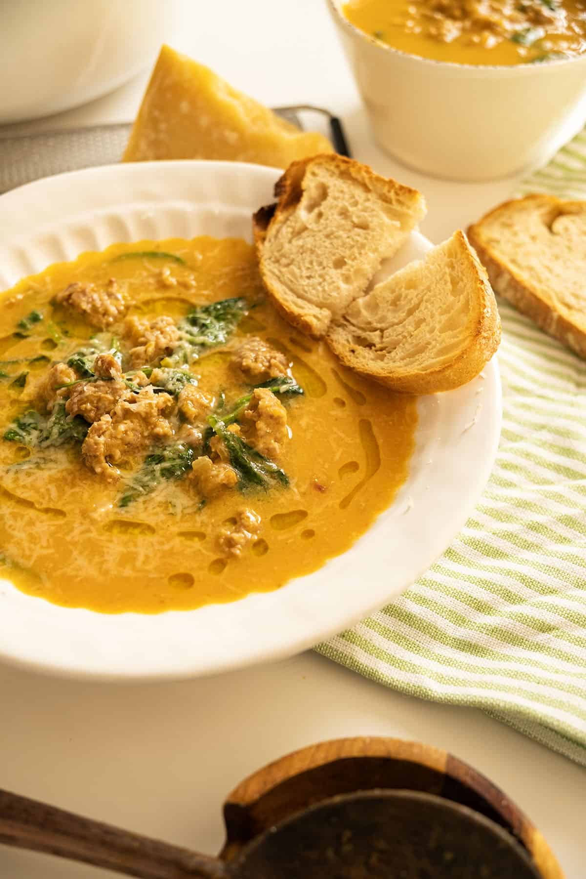 Butternut squash soup with sausage in a bowl and side of crusty Italian bread.