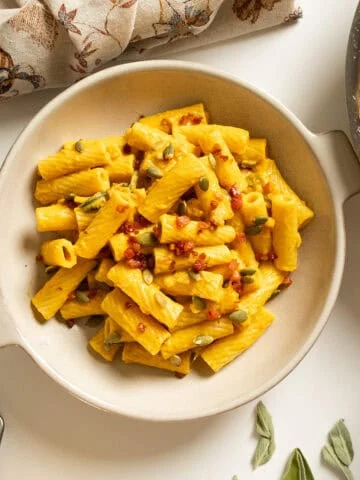 Pumpkin pasta in a bowl topped with pumpkin seeds and pancetta.