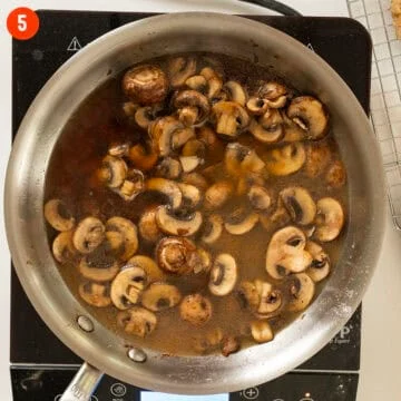 Mushrooms simmering in marsala wine and broth in a pan.