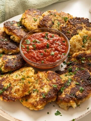 Fried cauliflower cakes on a plate with marinara sauce.