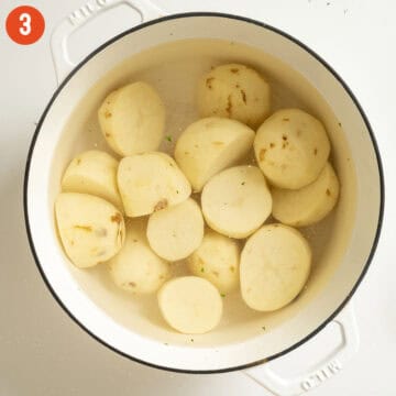 Halved and peeled potatoes in a pot water.