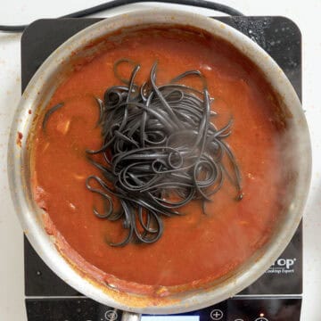 Adding squid ink pasta simmering with sauce and calamari.