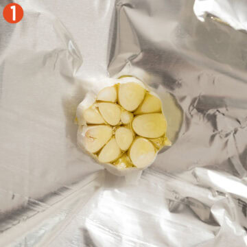 Garlic head cut in half in aluminum foil.