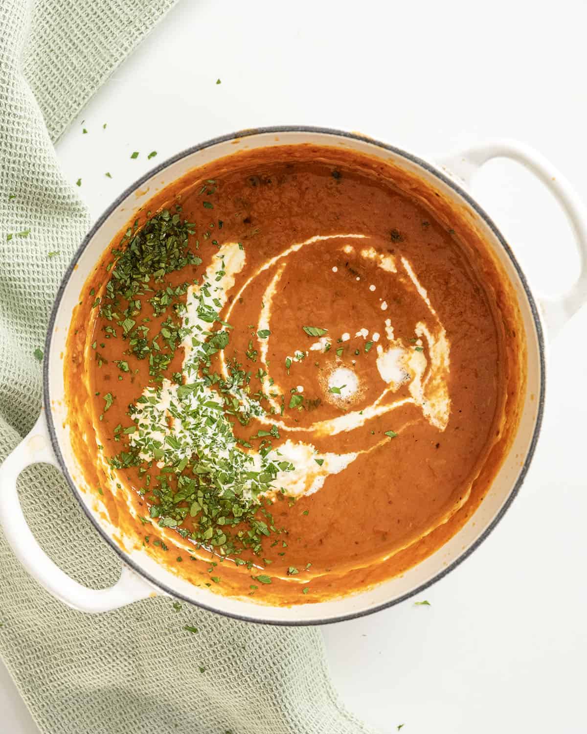 Roasted red pepper soup drizzled with cream and garnished with parsley.