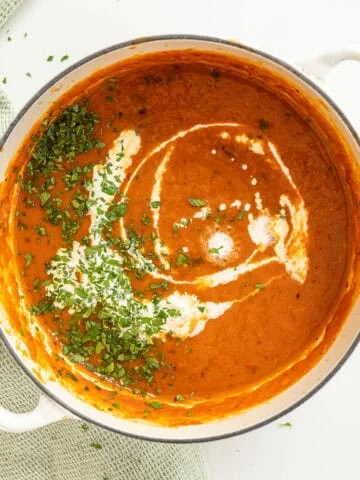 Roasted red pepper soup drizzled with cream and garnished with parsley.