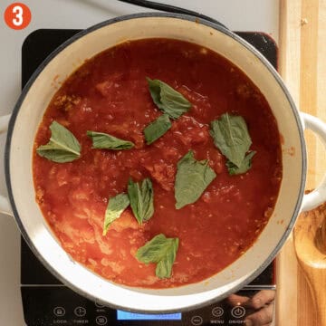 Simmering tomatoes and basil in a pan.